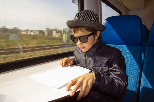 Handsome boy with sunglasses rides on a train reading from the paper