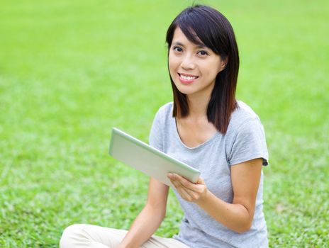 Asian woman setting on grass with tablet
