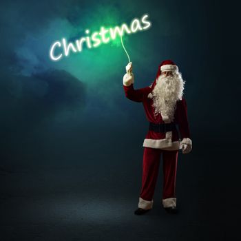 Santa Claus is holding a shining Christmas word sign on a string