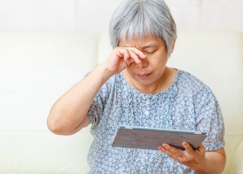 Asian old woman using digital tablet with tired eyes