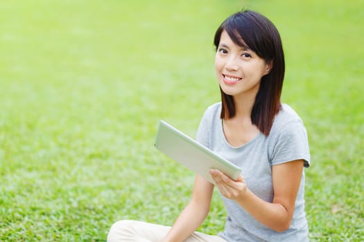Asian woman sitting on the lawn with tablet