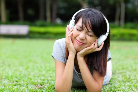 Asian woman listen to song lying on grass