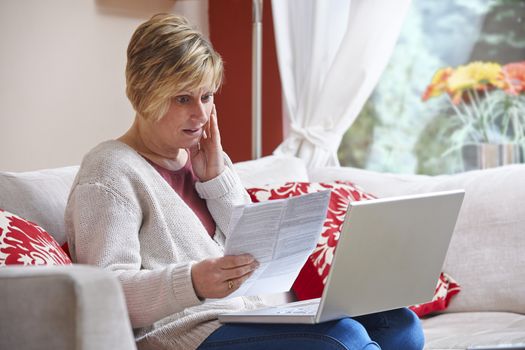 Worried woman looking at bill while on computer at home