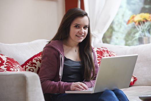 teenage girl smiling at camera while on laptop at home
