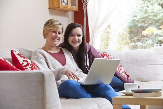 Mother and daughter enjoying surfing on the net while relaxing at home with coffee