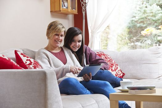 Mother and daughter enjoying surfing on the net while relaxing at home with coffee