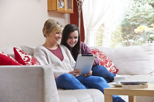 Mother and daughter enjoying surfing on the net with tablet  while relaxing at home with coffee