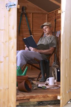 Man reading book while sitting in deckchair in his garden shed