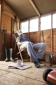 Man sitting in deckchair falling asleep in the shed while reading book