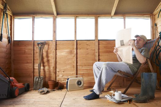 Man checking share prices while sitting in deckchair in his garden shed