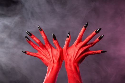 Red devil hands with sharp black nails, extreme body-art, studio shot over smoky background 
