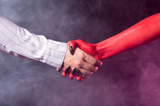 Businessman making a deal with devil, studio shot on smoky background 