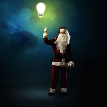 Santa Claus is holding a shining lamp on a string