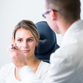 optometry concept - pretty young woman having her eyes examined by an eye doctor