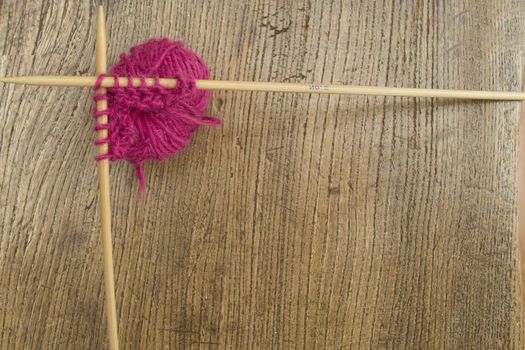 Pink wool and knitting needle boreder on a wooden background