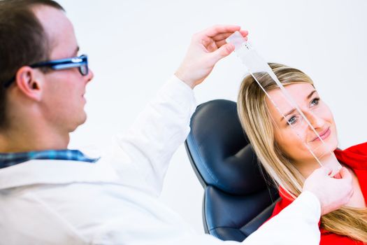 Optometry concept - pretty young woman having her eyes examined by an eye doctor (color toned image; shallow DOF)