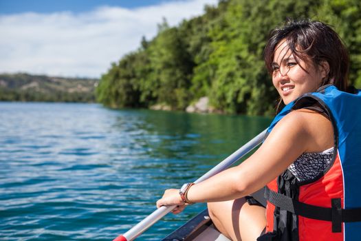 Pretty, young woman on a canoe on a lake, paddling, enjoying a lovely summer day