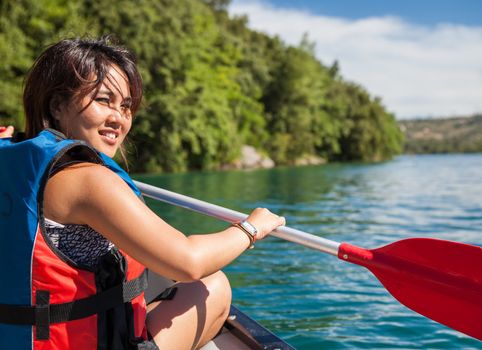 Pretty, young woman on a canoe on a lake, paddling, enjoying a lovely summer day