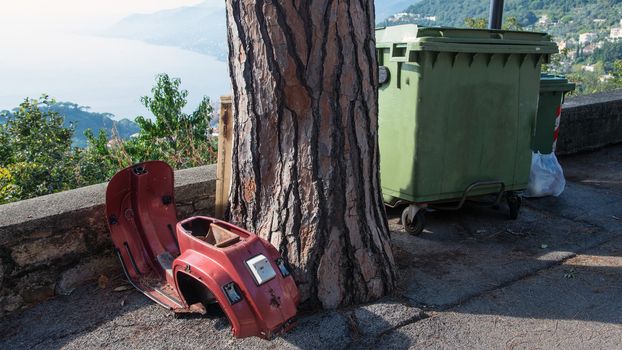 carcass abandoned scooter near a tree and a garbage dumpster