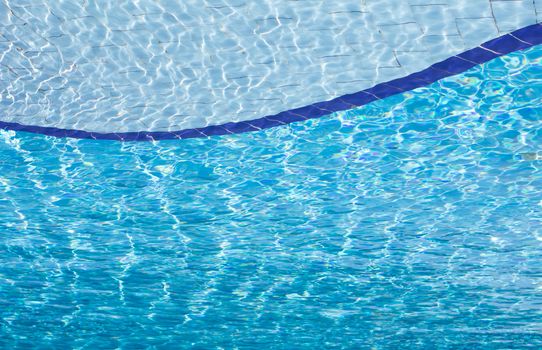 Background of clear blue water with sun reflections in an outdoor swimming pool.