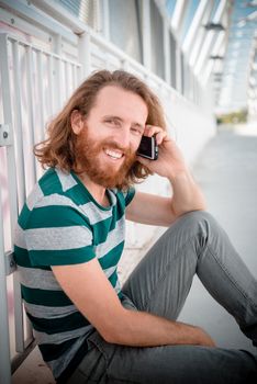 stylish hipster model with long red hair and beard lifestyle on the phone in the street