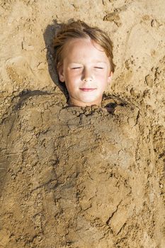 happy boy dig oneself in the sand at the beach and has fun