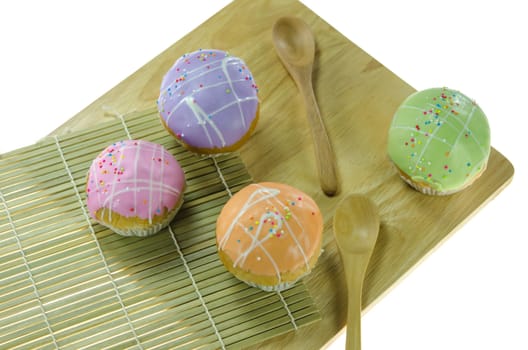 top view four cupcake with colorful sprinkles  and wooden spoon on wooden board over white background