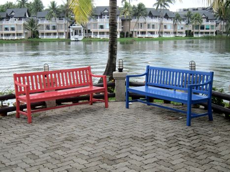 Red and blue park benches by a lake.