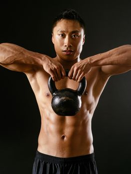 Photo of an Asian male exercising with a kettle bell over dark background. 