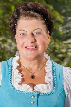 Portrait of a smiling attractive middle-aged lady in a dirndl with neatly braided hair looking at the camera