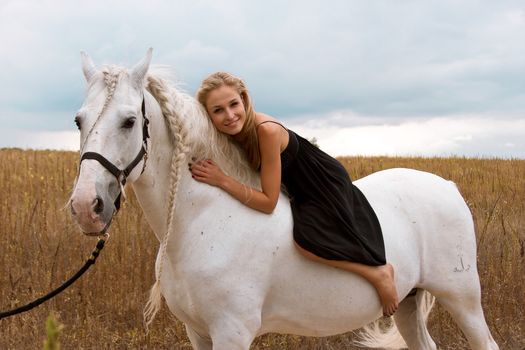 girl in the black dress is riding on a white horse