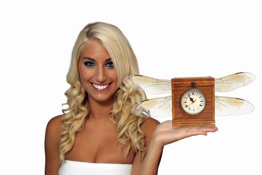 An extraordinarily beautiful young blonde with a bright, warm smile, holding an antique clock with wings in her extended left hand.