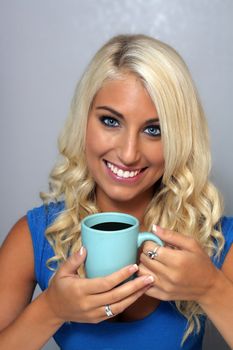 Close-up of an extraordinarily beautiful young blonde with a bright, warm smile and a cup of coffee.