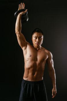 Photo of an Asian male exercising with a kettle bell over dark background. 