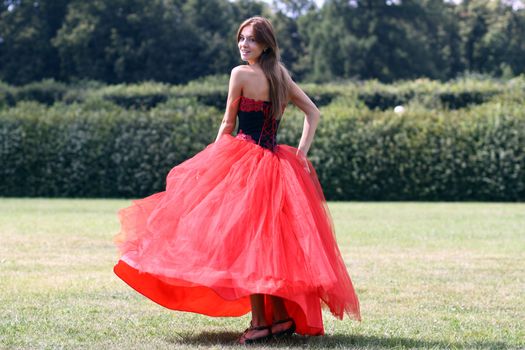 Beautiful woman in a red dress walking on meadow in park
