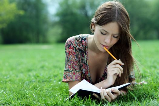 Young beautiful woman lays on a grass in park with a diary in hands