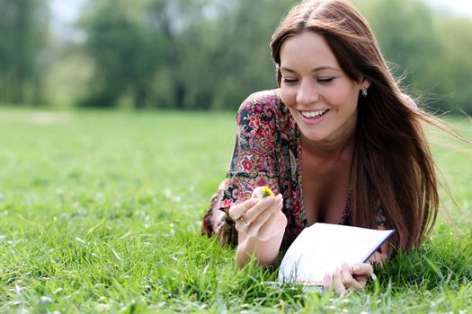 Young beautiful woman lays on a grass in park with a diary in hands