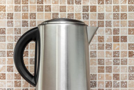 Metal electric kettle on kitchen tile background.