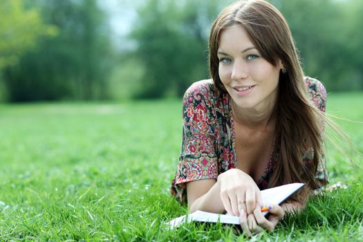 Young beautiful woman lays on a grass in park with a diary in hands