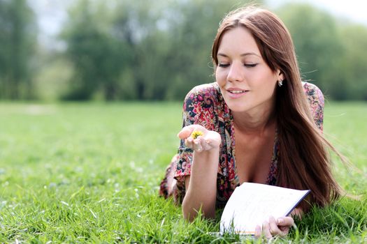 Young beautiful woman lays on a grass in park with a diary in hands