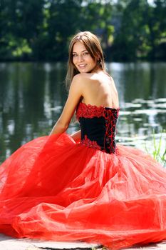 Smiling woman in a red dress sitting near river