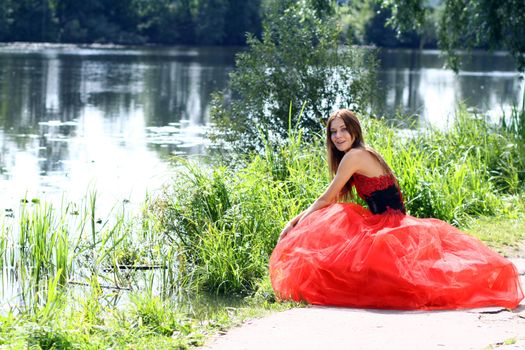 Smiling woman in a red dress sitting near river