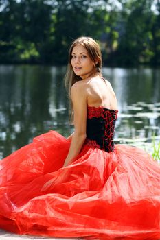 Smiling woman in a red dress sitting near river