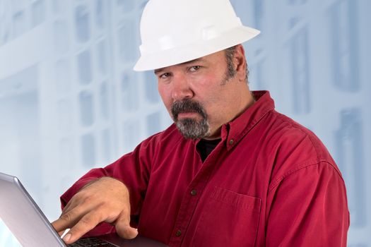 Hardhat technician looking at camera trustfully while working on the laptop