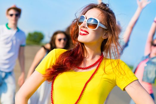 stylish young woman in sunglasses on the background of blue sky and friends