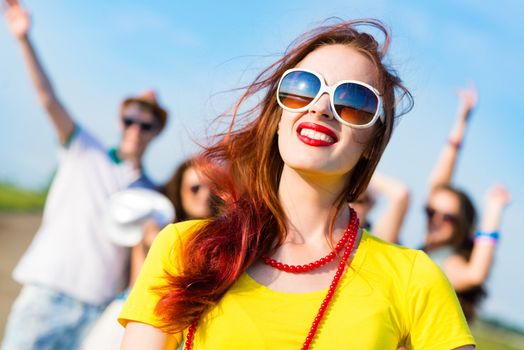 stylish young woman in sunglasses on the background of blue sky and friends