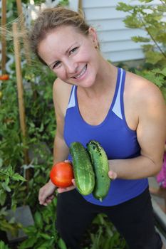 Middle aged women harvesting her organic grown tomatoes and cucambers from her green garden.