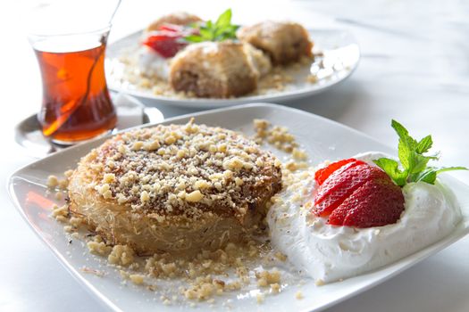 Kunefe and hot turkish tea served with Strawberry and full fat cream and garnished with mint leaves, baklava at the background