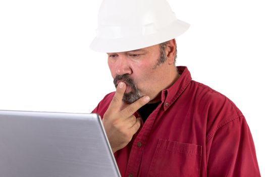 Hardhat worker working or surfing with his laptop, he has a puzzled look, he is wearing red shirt and isolated on white background, copy space on hardhat and laptop