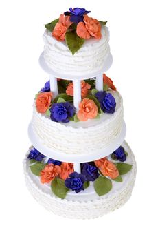 Isolated three tier ruffled white wedding cake decorated with orange and purple roses and green leafs